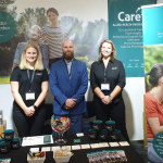 a male in suit and care workers standing behind Care Squared booth