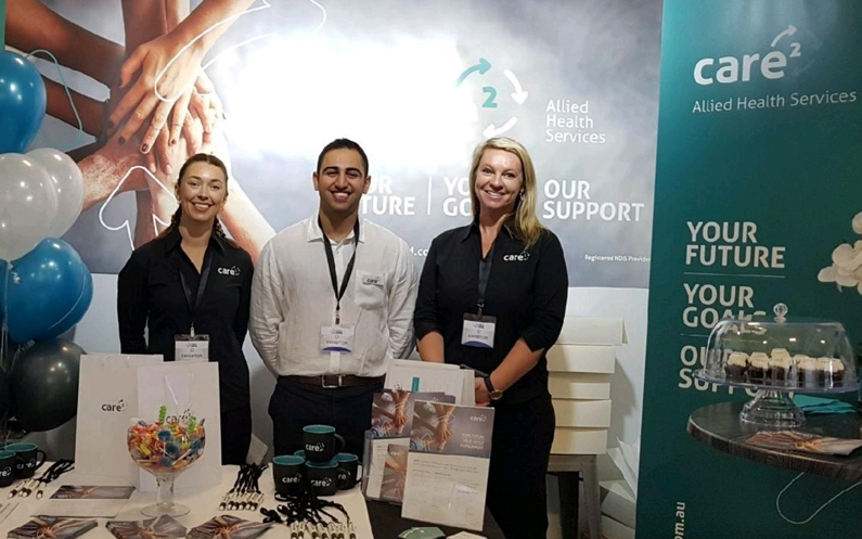 Care workers standing behind a Care Squared booth smiling for photo